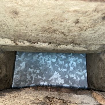 View down a small rectangular stone or concrete shaft with a reflective metallic bottom.