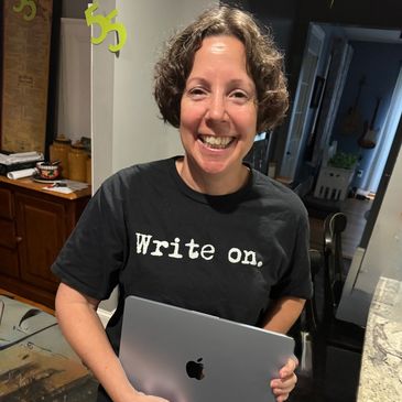 Smiling person holding a laptop and wearing a "Write on." t-shirt.