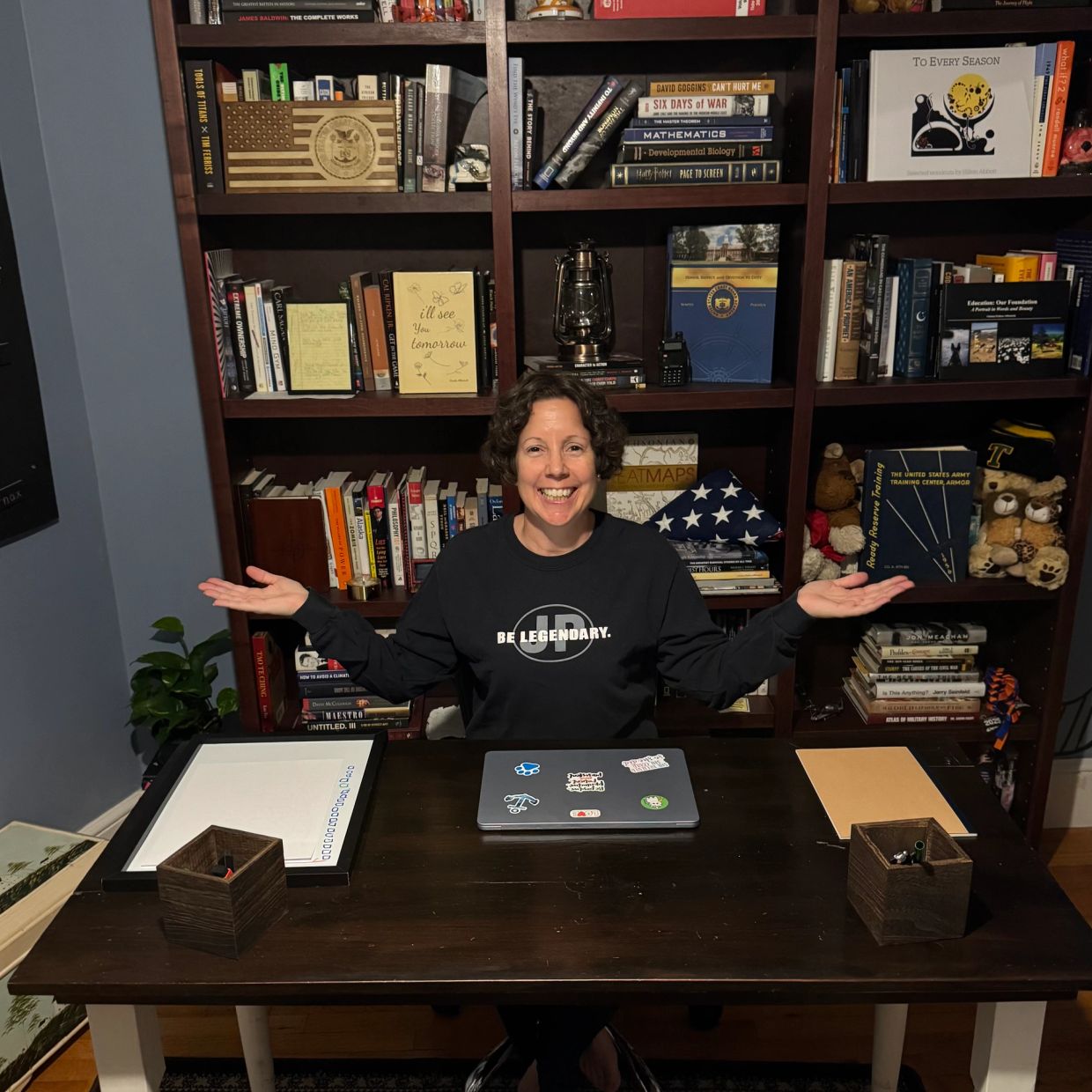 Woman smiling at desk with bookshelf background.