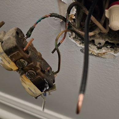 Exposed, damaged electrical outlet with frayed wires.