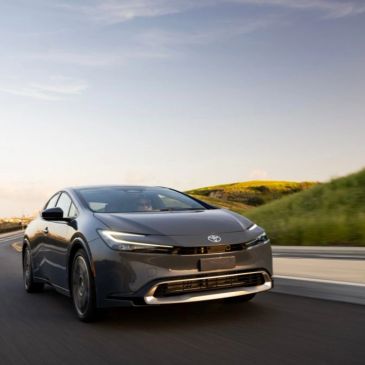 A sleek gray Toyota sedan driving on a winding road during sunset.