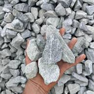 Hand holding several rough gray stones against a background of similar stones.