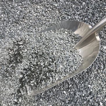 Metal scoop filled with small gray gravel on a gravel pile.