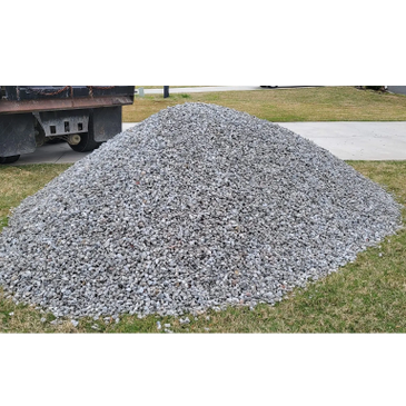 A large pile of gray gravel on grass near a driveway.