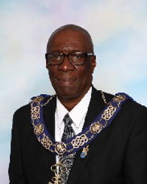 Elderly man wearing a ceremonial chain and suit.
