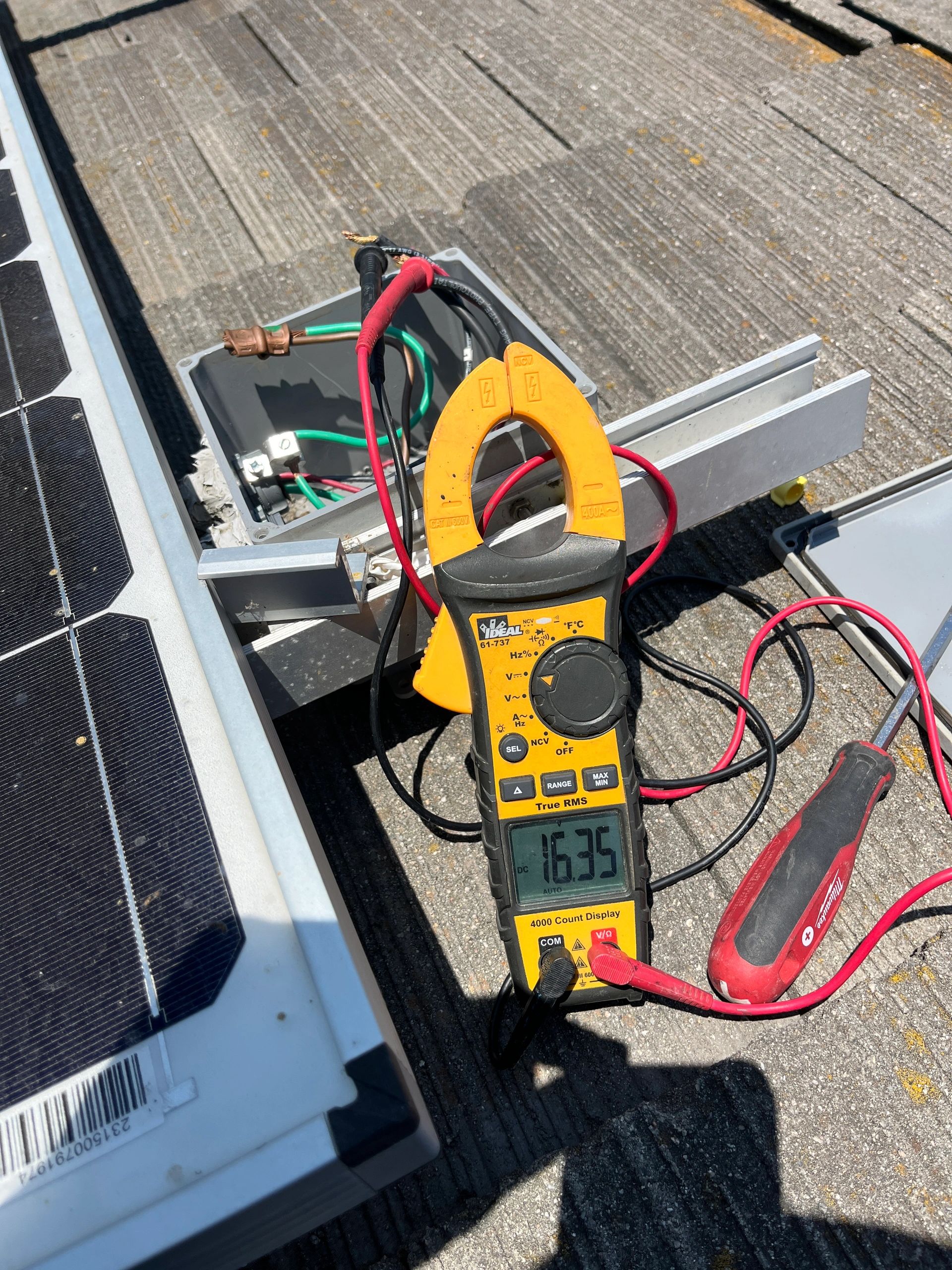 Clamp meter measuring voltage on a solar panel setup outdoors.