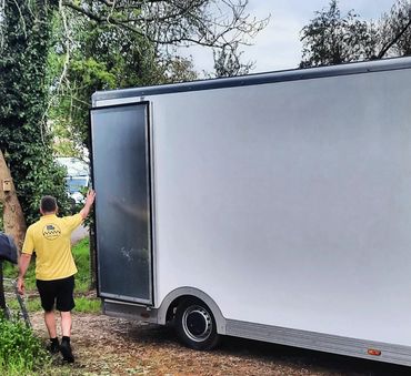 Man in yellow shirt opening side door of a large white trailer outdoors.