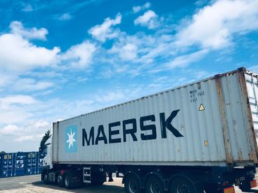A large Maersk shipping container on a truck under a bright blue sky.