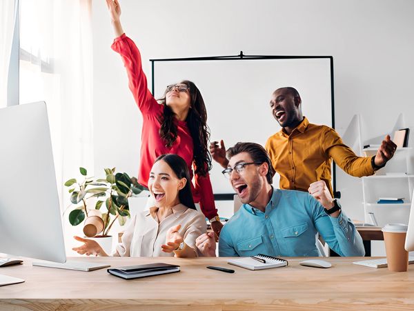 Four overjoyed colleagues celebrating success in an office.