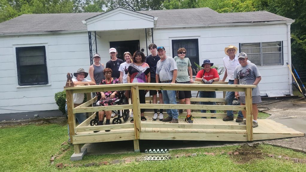 Group of people gathered on a newly built wooden wheelchair ramp in front of a house.