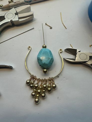 Jewelry making workspace with tools and a partially assembled necklace featuring a large turquoise bead.