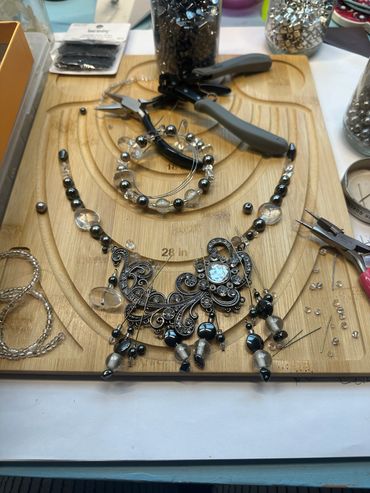 Jewelry-making tools and beads arranged on a wooden bead board.