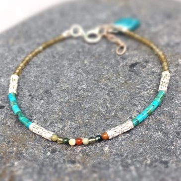 Delicate beaded bracelet with turquoise and silver accents on gray stone.