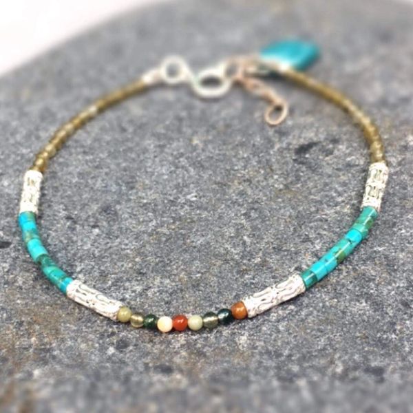 Delicate beaded bracelet with turquoise and silver accents on gray stone.