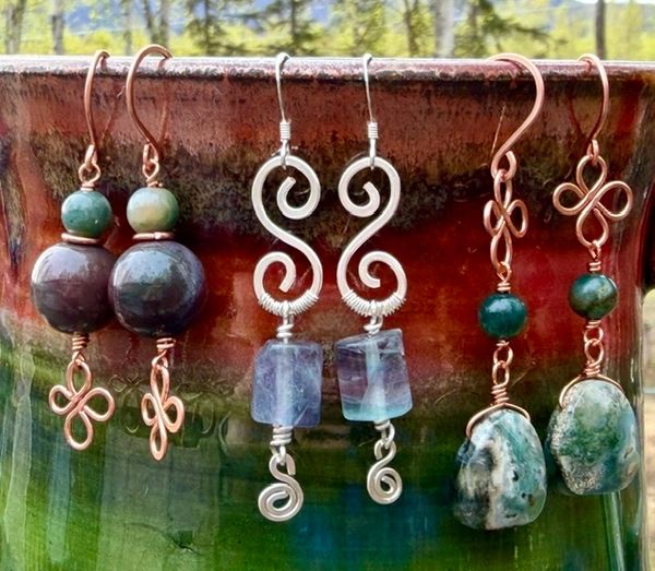 Handcrafted earrings with stones and intricate wire designs displayed on a ceramic pot.