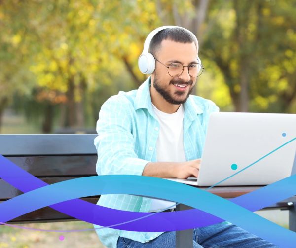 young Asian man with headphones on a bench with is laptop receiving online coaching