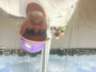 Man in purple cap takes selfie on a sailboat with two people in the background.