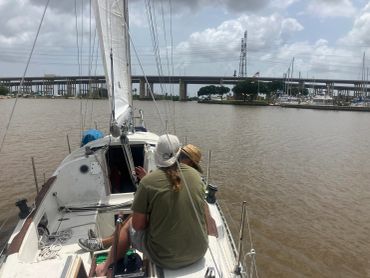 Two people sailing on a calm river near a bridge and marina.