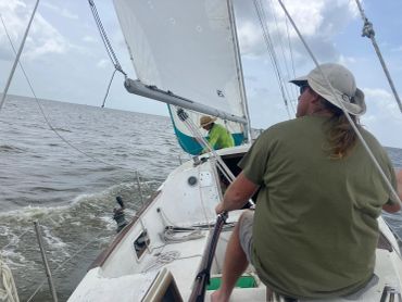 Two people sailing on a small boat under a cloudy sky.