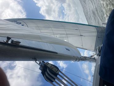 View looking up the mast and sails of a sailboat on a partly cloudy day.