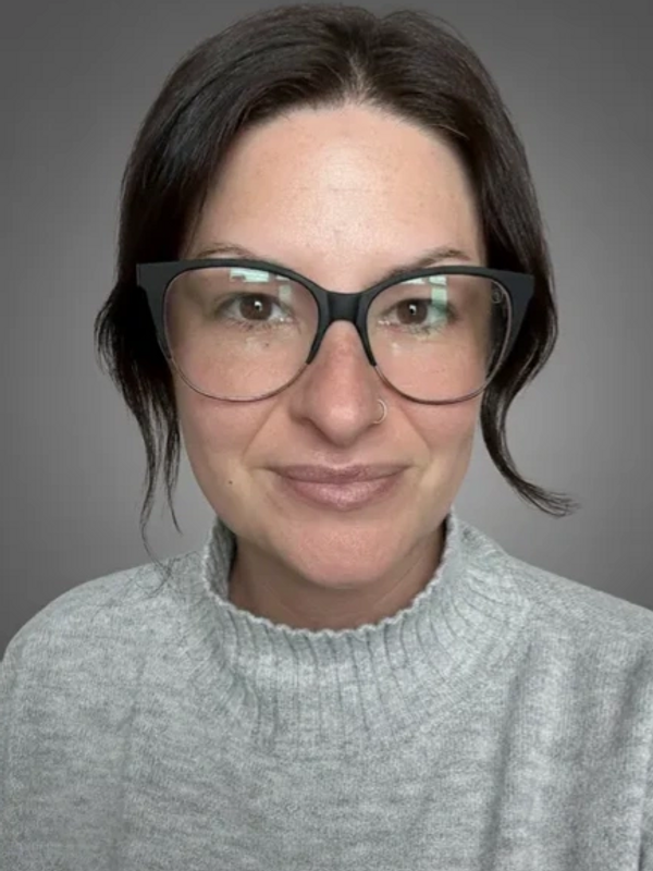 Woman with dark hair, glasses, and a gray sweater smiling gently.