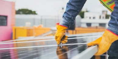 Worker installs solar panel with safety gloves and vest.