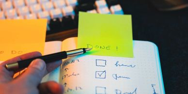 Hand holding pen over checklist with sticky note reading 'DONE!'