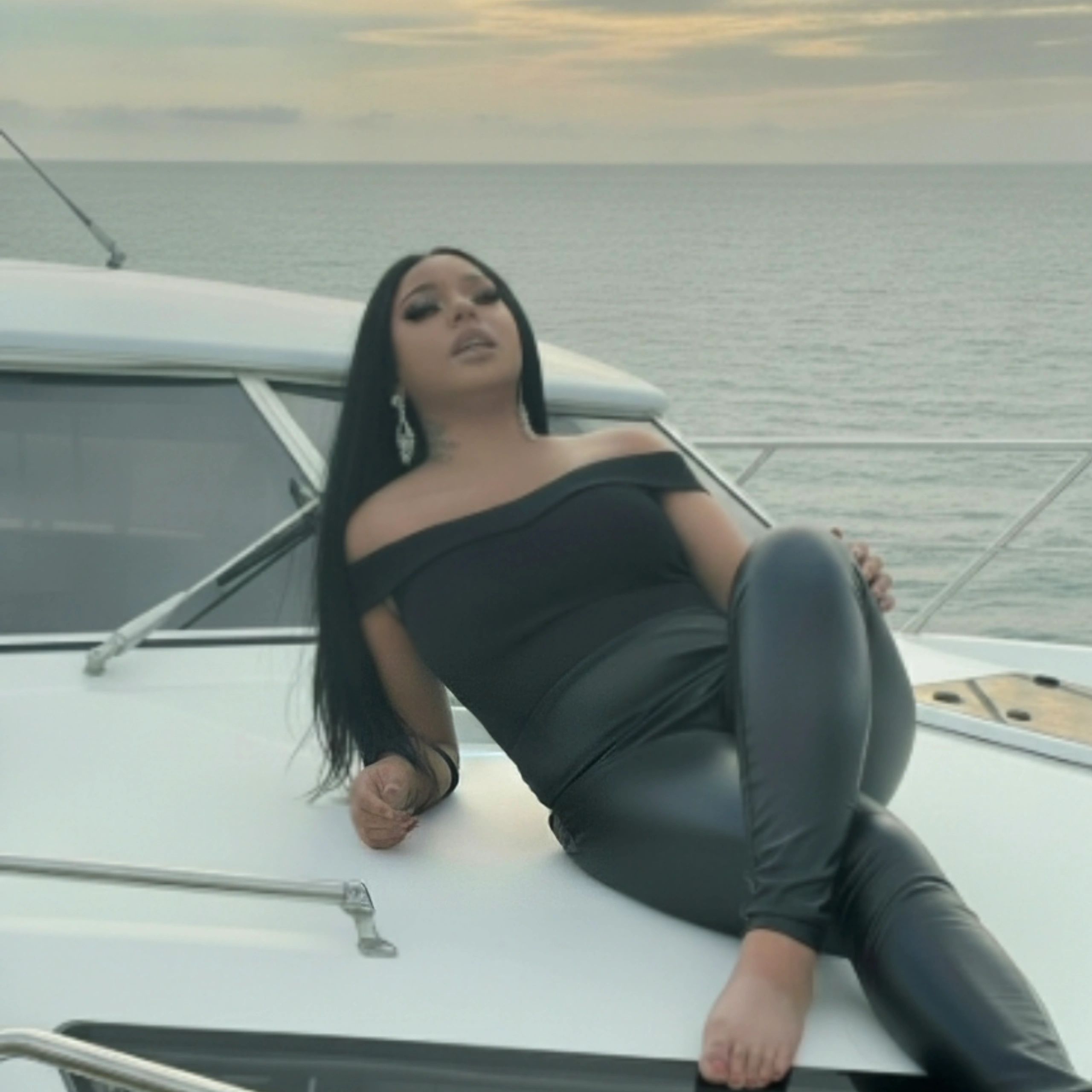 Woman in black outfit reclining on a yacht with ocean background.