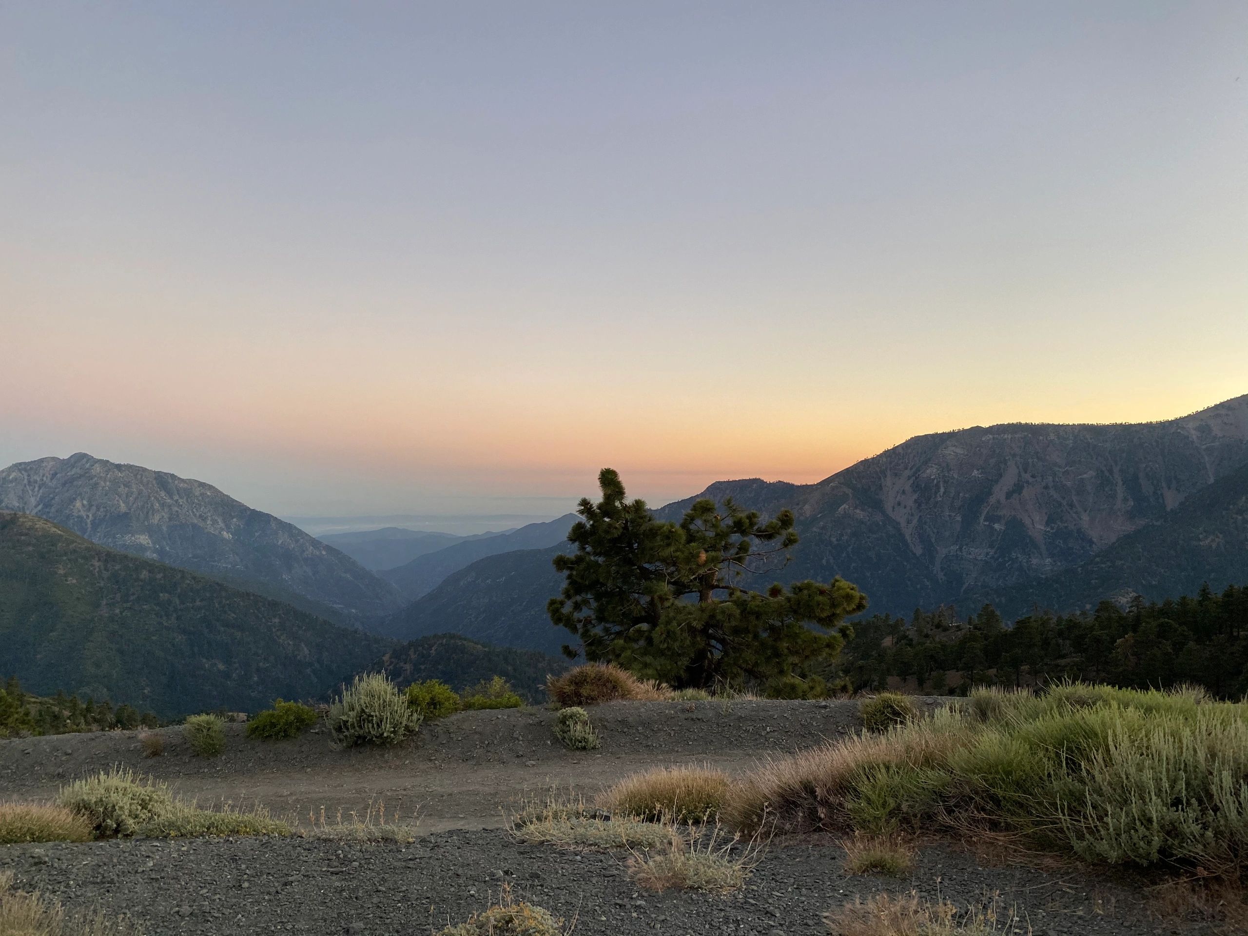 Sunset over a mountainous landscape with sparse vegetation.