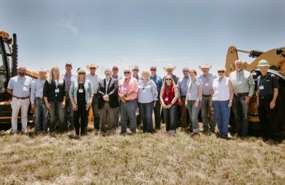Group of professionals standing outdoors in front of construction equipment.