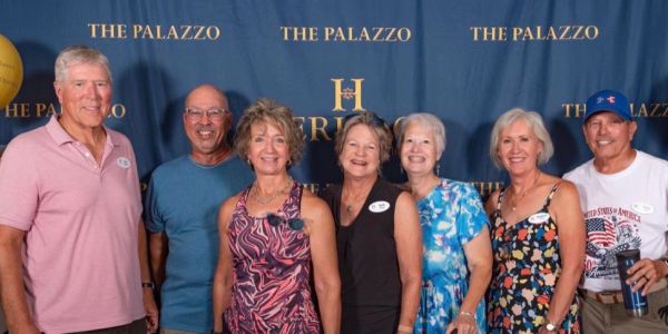 Group of seven smiling adults posing in front of a backdrop.