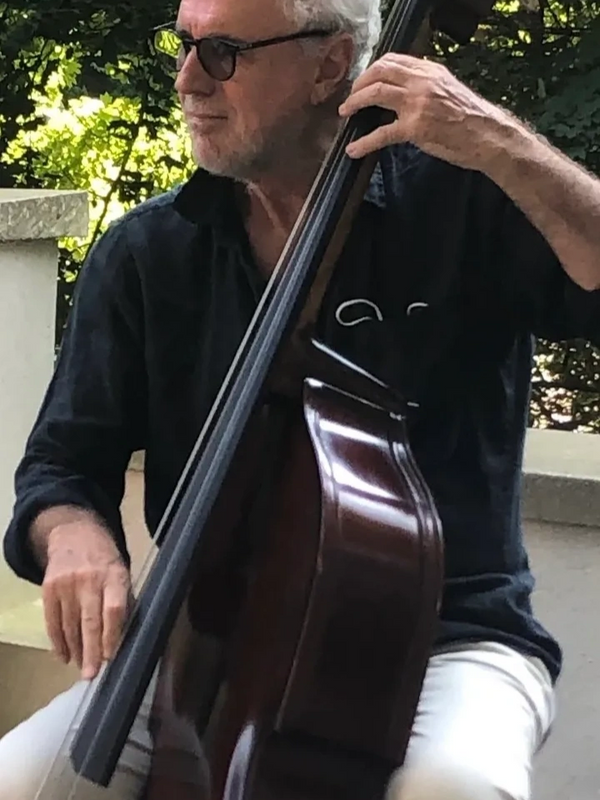 Man in sunglasses playing a double bass outdoors.