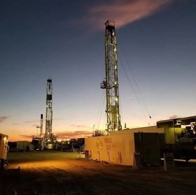 Oil drilling rigs at sunset with lights on.