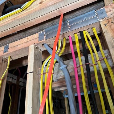 Colorful electrical cables organized and secured inside wooden framing.