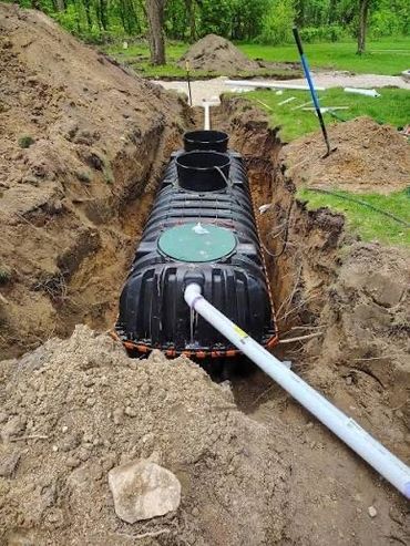 A black septic tank being installed in a dug trench outdoors.
