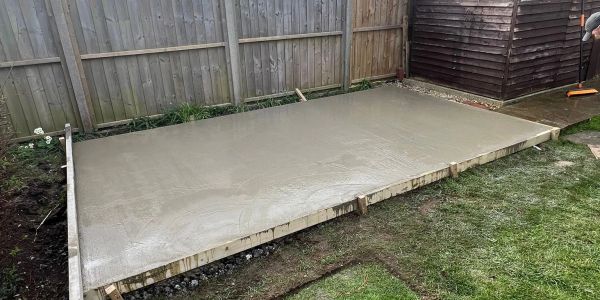 Freshly poured concrete slab in a backyard garden area.