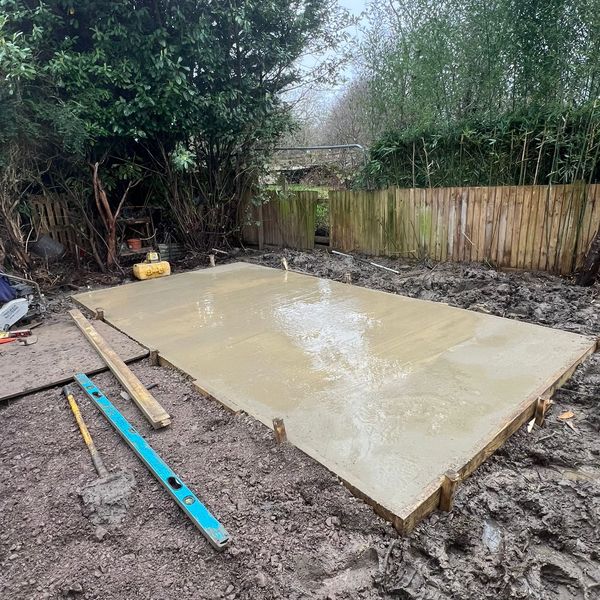 Freshly poured concrete slab in a muddy backyard under construction.