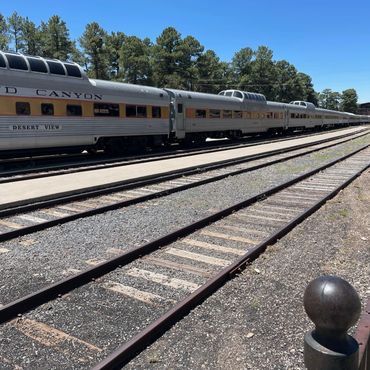 Grand Canyon Desert View train parked by the tracks under a clear blue sky.