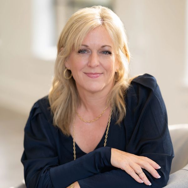 Confident woman with blonde hair and a warm smile, dressed in a dark blouse.