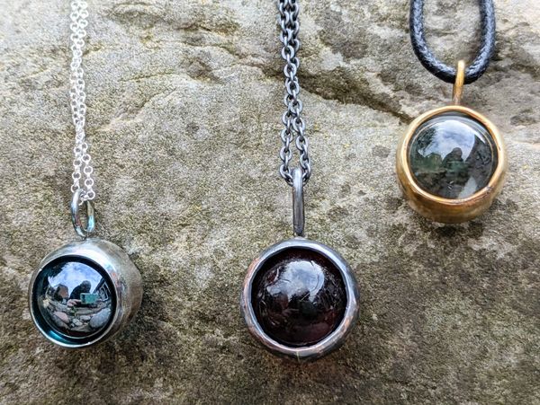 Three round pendant necklaces on stone surface.