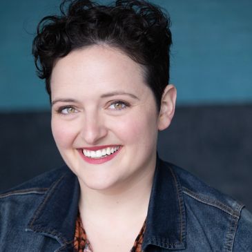 Smiling woman with short curly hair in a denim jacket.