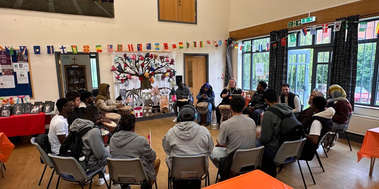 Group of people sitting in a circle playing drums inside a decorated room.