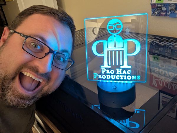 Man excitedly posing next to a glowing Pro Hac Productions sign.