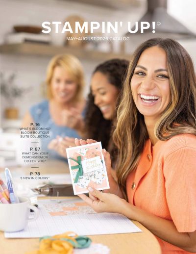 Three women crafting happily, one showing a handmade card in an orange sweater.