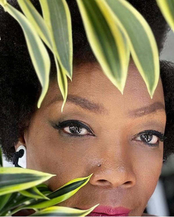 Close-up of a woman peeking through green leaves with expressive eyes and makeup.