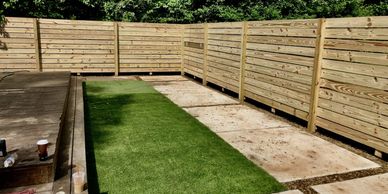 A backyard with wooden fencing and a strip of green grass.