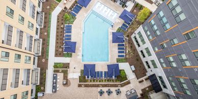 Aerial view of a swimming pool surrounded by lounge chairs and umbrellas in a residential complex.