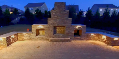 Outdoor stone fireplace with warm lighting at dusk in a backyard.