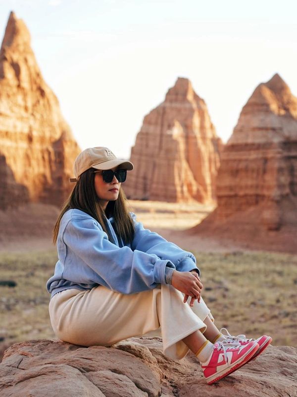 Woman in casual wear sitting on a rock with sandstone formations in the background.