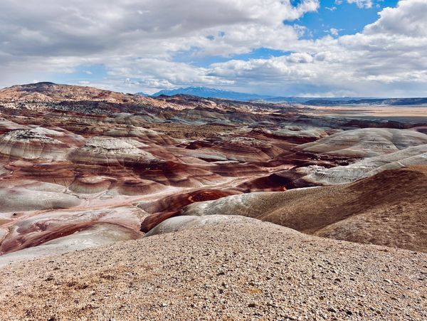 Colorful rock formations stretch across a vast desert landscape under a partly cloudy sky.